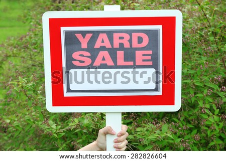 Wooden Yard Sale sign in female hand over green grass background