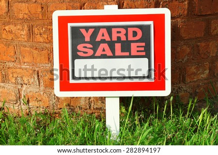 Wooden Yard Sale sign in green grass on red brick wall background