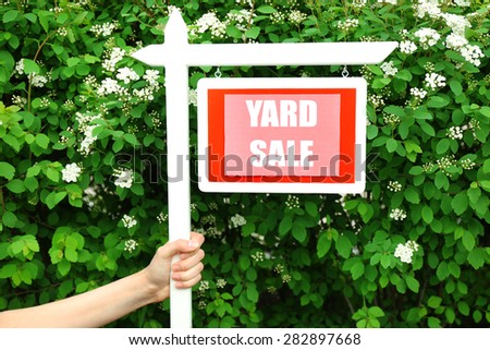 Wooden Yard Sale sign in female hand over green bush and flowers background