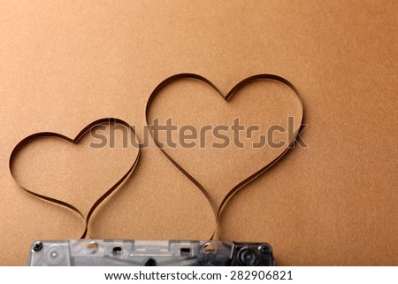 Audio cassette with magnetic tape in shape of hearts on brown background