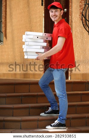 Delivery boy with cardboard pizza box near house of customer, outdoors