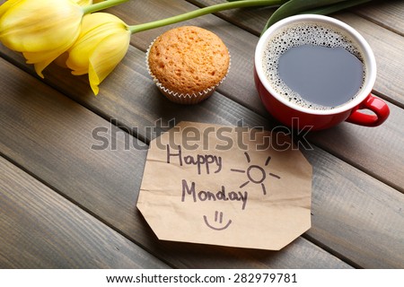 Cup of coffee with fresh cupcake, tulips and Happy Monday massage on wooden background