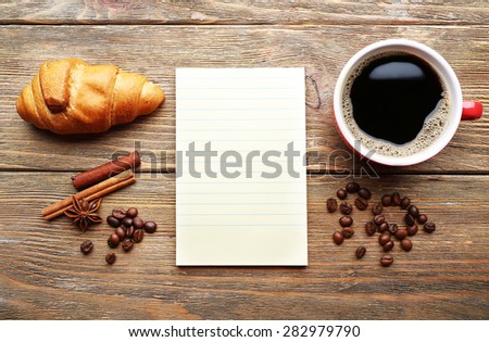 Cup of coffee with fresh croissant and blank sheet of paper on wooden table, top view