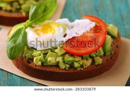 Tasty sandwich with egg, avocado and vegetables on paper napkin, on color wooden background