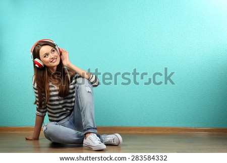 Young woman sitting on floor with headphones on turquoise wallpaper background