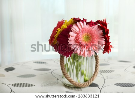 Glass vase of colorful gerbera flowers on table on curtains background