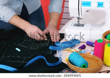 Male dressmaker drawing line on fabric on table close-up