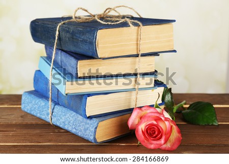 Tied books with pink rose on wooden table, closeup
