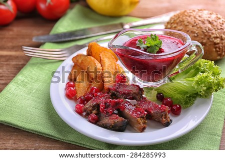 Beef with cranberry sauce, roasted potato slices on plate, on wooden background