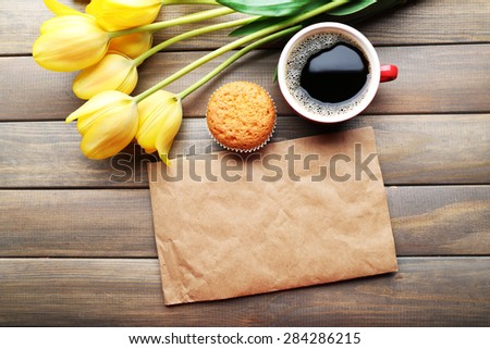 Cup of coffee with fresh cupcake, tulips and blank sheet of paper on wooden background