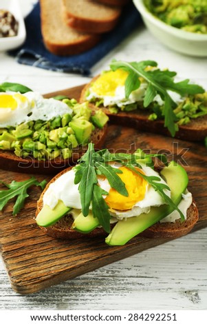 Tasty sandwiches with egg, avocado and vegetables on wooden background