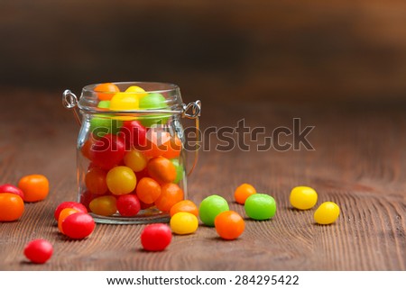 Colorful candies in jar on table on wooden background