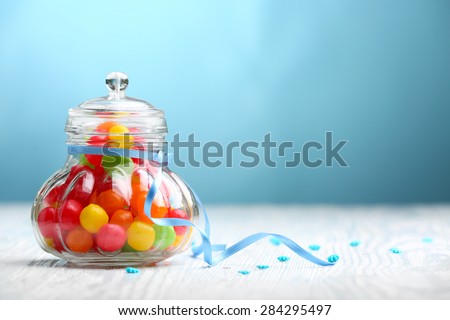 Colorful candies in jar on table on blue background