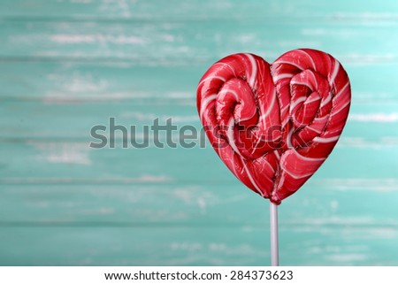 Bright lollipop in shape of heart on wooden background