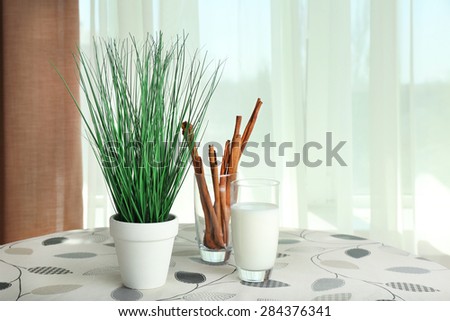 Green plant with glass of milk and cinnamon sticks on table on curtains background