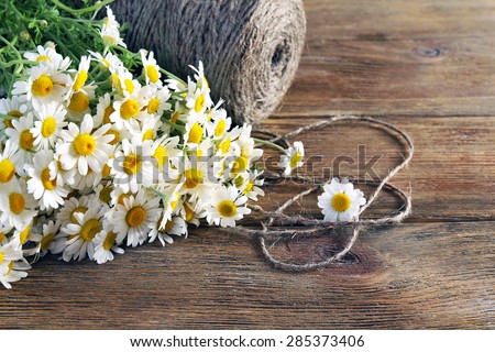 Beautiful bouquet of daisies with twine on wooden background