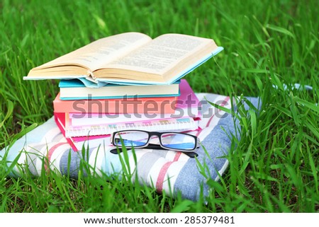 Books and glasses on pillow on grass close-up