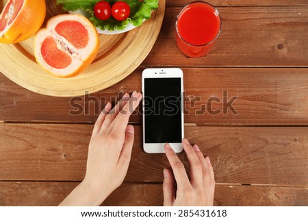 Food and mobile phone in female hands on wooden background