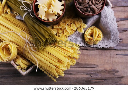 Different types of pasta in wicker basket with fabric on rustic wooden table background