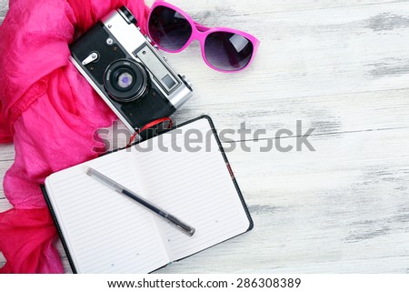 Set of tourist with open notebook, retro camera, pen and sunglasses on wooden table background