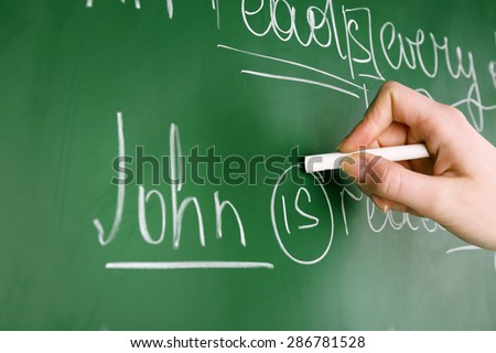 Teacher hand writing grammar sentences on blackboard background