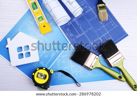 Construction instruments, plan and brushes over house plan on wooden table background