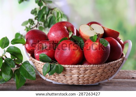 Red apple in wicker basket on wooden table, on blurred background