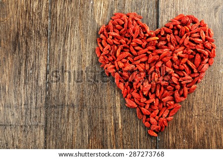 Goji berries arranged in heart shape on wooden background