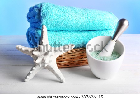 Rolled towels in wicker basket with starfish and sea salt on wooden table and light colorful background