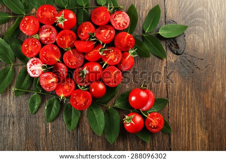 Cherry tomatoes arranged in heart shape with green leaves on wooden background