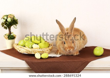Cute red rabbit with Easter eggs on shelf on light wallpaper background