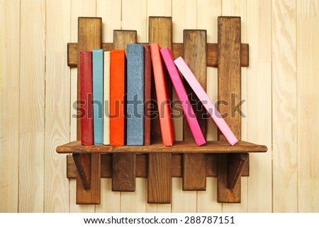 Colorful books on shelf on wooden wall background