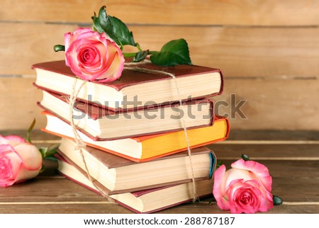 Tied books with pink roses on wooden background