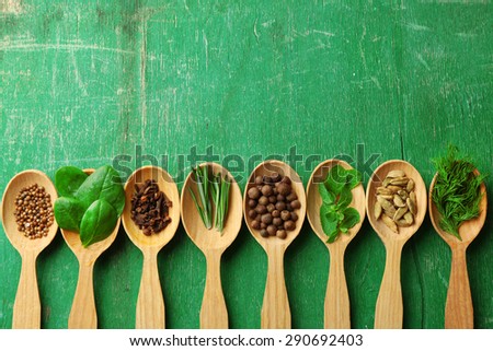 Wooden spoons with fresh herbs and spices on color wooden background