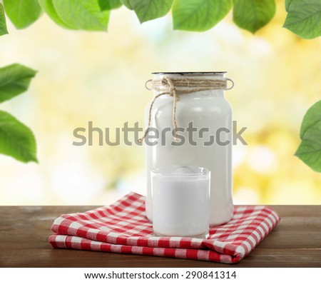 Retro can for milk and glass of milk on wooden table, on nature  background