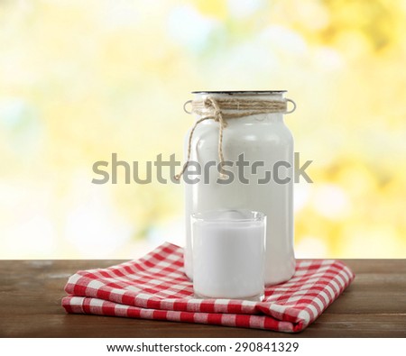 Retro can for milk and glass of milk on wooden table, on bright background