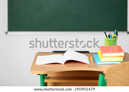 Wooden desk with stationery and chair in class on blackboard background