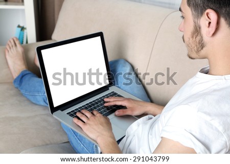 Handsome young man sitting on sofa and using laptop in room
