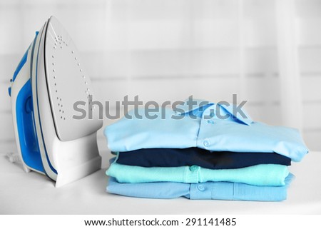 Pile of clothes and electric iron on fabric background