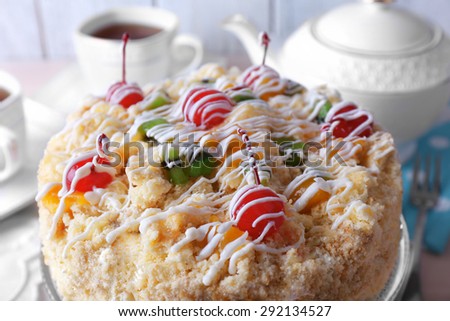 Butter cake with cherries on stand and table setting, on color wooden background