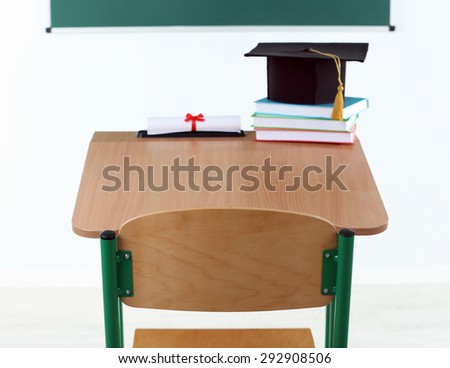 School desk with master hat, stack of books and diploma in classroom