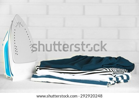 Pile of clothes and electric iron on brick wall background