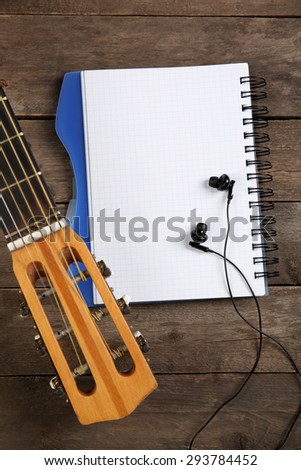 Music recording scene with guitar, memo pad and earphones  on wooden background