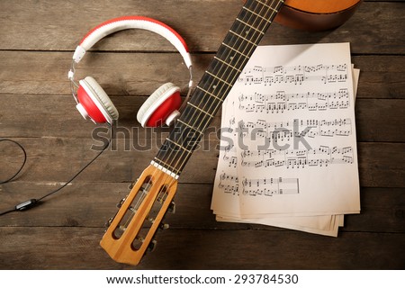 Music recording scene with guitar, music sheets and headphones on wooden table, closeup