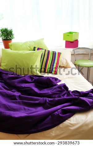 Comfortable bed with colorful pillows and purple blanket in bedroom