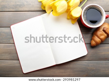 Cup of coffee with fresh croissant, tulips and blank sheet of paper on wooden background