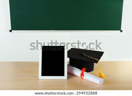 Graduation cap with tablet and diploma on table in class