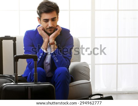 Business man with suitcases sitting on sofa in hall