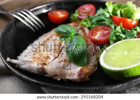 Dish of fish fillet with salad and lime on dripping pan close up
