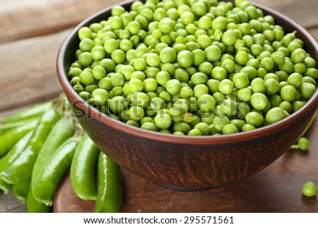 Fresh green peas in clay bowl on wooden cutting board, closeup